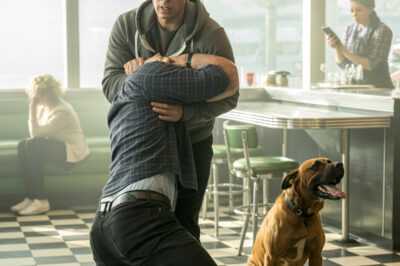 El golpe apagó todas las conversaciones como si alguien hubiese arrancado el cable de la realidad. Las tazas vibraron, una niña ahogó un grito, y el olor a café se mezcló con el del miedo. Nadie se movió. Nadie… hasta que la campanilla tintineó y entraron un hombre con sudadera gris y un perro que parecía hecho de acero. Lo que siguió no fue una pelea; fue una lección de control, una verdad que destapó años de cobardía y una ciudad aprendiendo a respirar sin miedo.